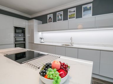A modern kitchen with white cabinets a sink a built in oven and a bowl of fruit on the countertop at Lake House Loft in Bowness-On-Windermere