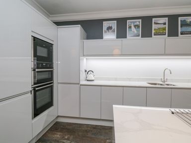 A modern kitchen with white cabinets built in ovens and a kettle on the countertop at Lake House Loft in Bowness-On-Windermere