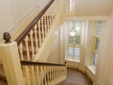 A staircase with carpeted steps and white wooden railings near stained glass windows and a hanging light at Lake House Loft in Bowness-On-Windermere
