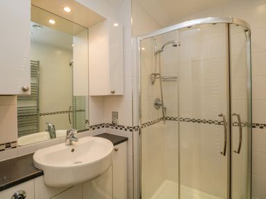 A bathroom with a sink, mirror, white cabinets, and a corner shower with glass doors at Lake House Loft in Bowness-On-Windermere