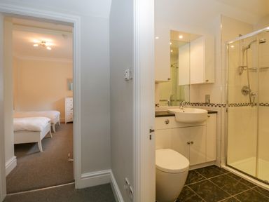A bathroom with toilet sink and shower next to a bedroom with two single beds at Lake House Loft in Bowness-On-Windermere
