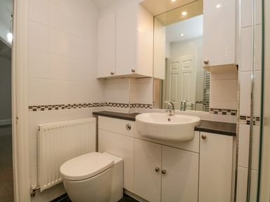 A bathroom with a toilet a sink a large mirror white cabinets and a radiator at Lake House Loft in Bowness-On-Windermere