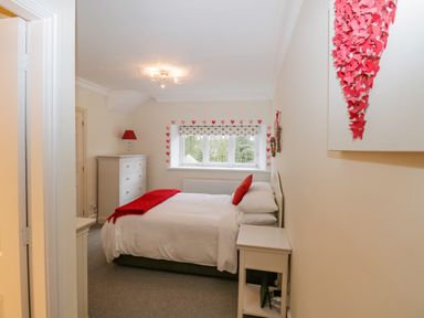 A bedroom with a bed with white linens and red accents a white dresser a window with heart decorations and a bedside table at Lake House Loft in Bowness-On-Windermere