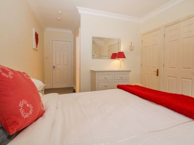 A bedroom with a bed with red pillows and blanket a dresser with a lamp and mirror at Lake House Loft in Bowness-On-Windermere
