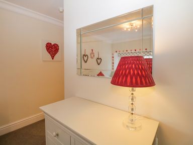A dresser with a red lamp and a mirror above it in a room with heart decorations at Lake House Loft in Bowness-On-Windermere