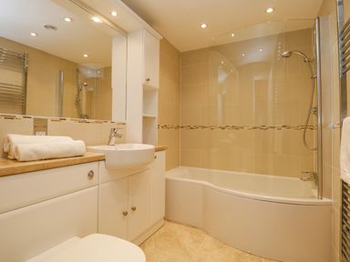 A bathroom with a bathtub shower combination a sink countertop with folded towels and a large mirror at Lake House Loft in Bowness-On-Windermere