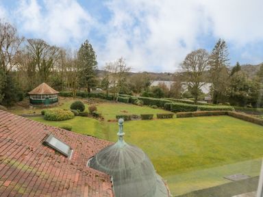 A garden with trimmed bushes a gazebo and a view of a lake beyond trees at Lake House Loft in Bowness-On-Windermere