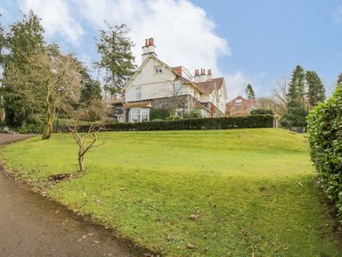 A large house with a sloped lawn and trees surrounding it at Lake House Loft in Bowness-On-Windermere