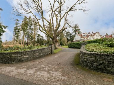 A driveway entrance with stone walls and a large tree leading to houses in the background at Meadowcroft