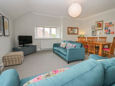 A living room with two blue sofas a wooden dining table with chairs a TV on a blue cabinet and wall art at Lake House Loft in Bowness-On-Windermere