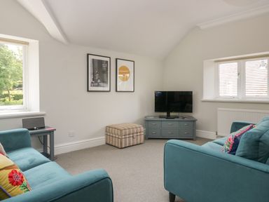 A living room with two teal sofas a striped ottoman a TV on a blue cabinet and two framed pictures on the wall at Lake House Loft in Bowness-On-Windermere