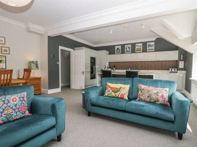 A living room with teal sofas and a kitchen area in the background at Lake House Loft in Bowness-On-Windermere