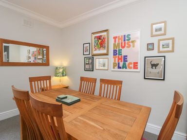 A dining room with a wooden table and six chairs a side table with a lamp and artwork on the walls at Lake House Loft in Bowness-On-Windermere