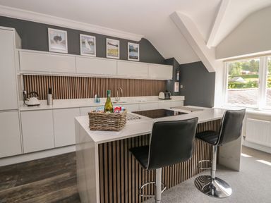 A modern kitchen with white cabinets a central island with two black bar stools and framed pictures on the wall at Lake House Loft in Bowness-On-Windermere