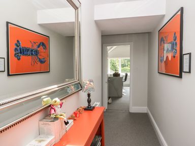 A hallway with a large mirror, an orange console table with books and a frog doll, lobster artwork on walls at Lake House Loft in Bowness-On-Windermere