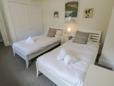 A bedroom with two single beds with pillows and rolled towels a nightstand with a lamp and closet doors at Lake House Loft in Bowness-On-Windermere