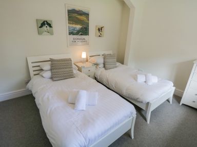 A bedroom with two single beds white bed frames bedside table lamp and wall art at Lake House Loft in Bowness-On-Windermere