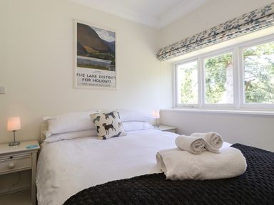 A bedroom with a bed with white linens and a dog print pillow next to windows at Lake House Loft in Bowness-On-Windermere