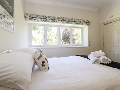 A bedroom with a bed with white sheets and pillows next to a window with floral blinds at Lake House Loft in Bowness-On-Windermere