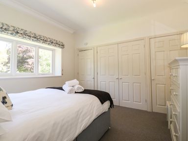 A bedroom with a bed with white linens and rolled towels near a window next to a wall with closed closets and a white dresser at Lake House Loft in Bowness-On-Windermere