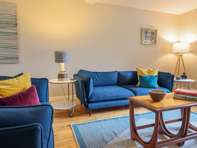 A living room with blue sofas yellow and red cushions a wooden coffee table and lamps at The Wardens House in Tregynon near Newtown