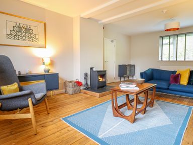 A living room with a blue sofa and wooden coffee table near a wood burning stove at The Wardens House in Tregynon near Newtown