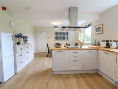 A kitchen with white cabinets wooden countertops a white refrigerator and a dining area at The Wardens House in Tregynon near Newtown