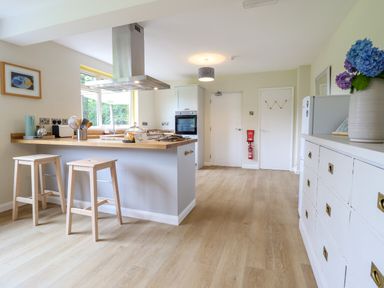A kitchen with wooden stools, a kitchen island, oven, cabinet, and a white dresser with flowers at The Wardens House in Tregynon near Newtown