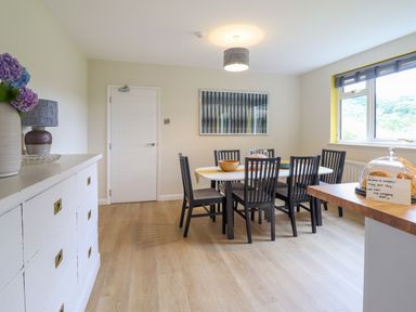 A dining room with a table and six chairs near a window and a sideboard with flowers at The Wardens House in Tregynon near Newtown