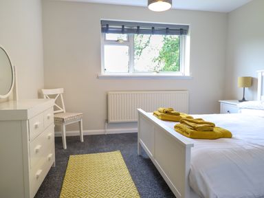 A bedroom with a bed a dresser a chair a window and a yellow rug at The Wardens House in Tregynon near Newtown