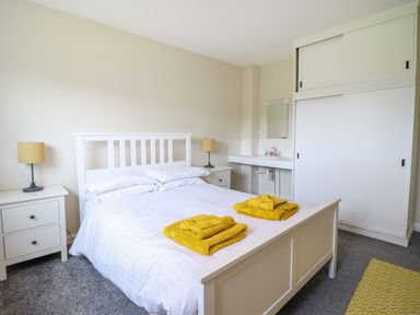 A bedroom with a white bed frame two yellow towels on the bed two matching bedside tables with lamps a sink and a wardrobe at The Wardens House in Tregynon near Newtown
