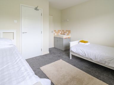 A bedroom with two single beds a door a small sink and a beige rug on the floor at The Wardens House in Tregynon near Newtown