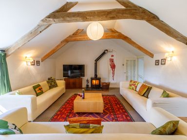 A living room with white sofas a red patterned rug wooden beams and a wood burning stove at Aarons Cottage in St Teath