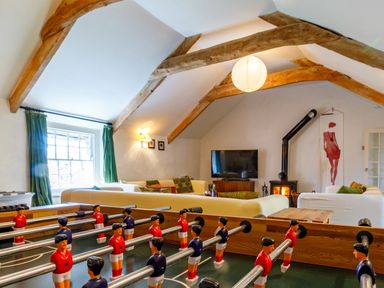 A room with a foosball table in front of sofas a wood burning stove and a television at Aarons Cottage in St Teath