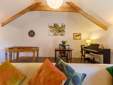 A room with a foosball table dartboard table with chairs piano and cushions on a sofa at Aarons Cottage in St Teath