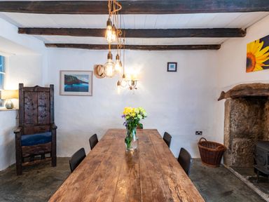 A dining room with a wooden table and chairs a vase with flowers hanging light bulbs and a stone fireplace at Aarons Cottage in St Teath