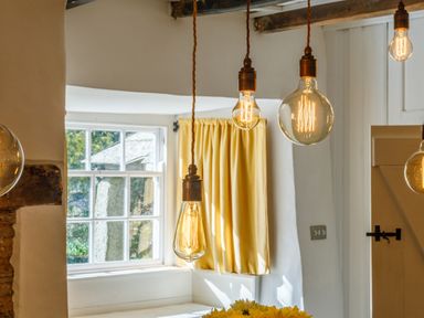 A room with hanging light bulbs yellow curtains and a window at Aarons Cottage in St Teath