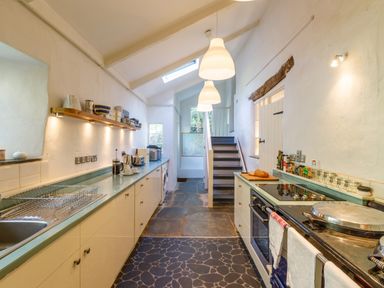 A kitchen with countertops a stove and stairs at Aarons Cottage in St Teath