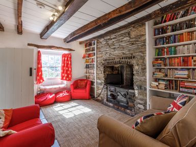 A living room with bookshelves a stone fireplace red chairs and a window with red curtains at Aarons Cottage in St Teath
