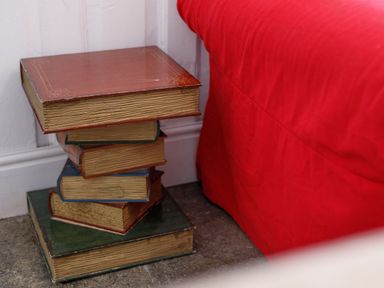 A stack of books arranged as a side table next to a bed with a red bedspread at Aarons Cottage in St Teath