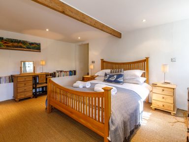 A bedroom with a wooden bed table lamps and a dresser with books at Aarons Cottage in St Teath