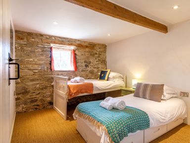 A bedroom with two single beds with colorful blankets and stone wall at Aaron's Cottage in St Teath