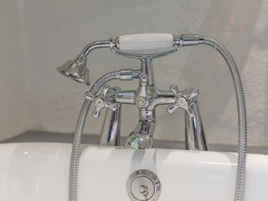 A bathtub faucet with hot and cold handles and a handheld shower head at Aarons Cottage in St Teath
