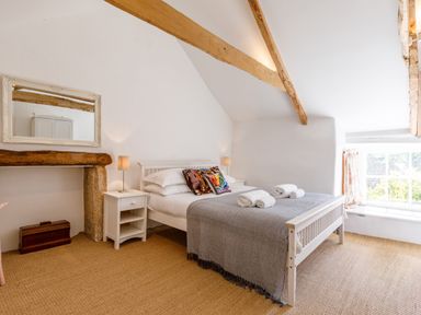 A bedroom with a white bed and colorful pillows by a window with exposed wooden beams at Aarons Cottage in St Teath