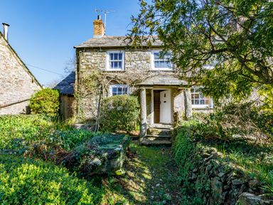 A stone cottage with an open door and garden pathway at Aarons Cottage in St Teath