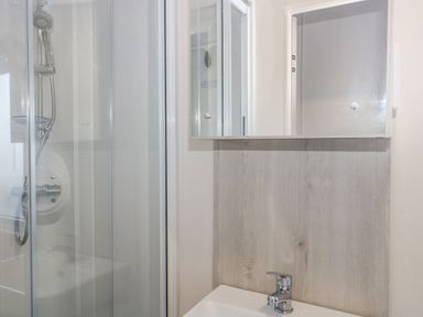 A bathroom with a shower enclosure a sink a mirror and wooden paneling at The Retreat in Otterton