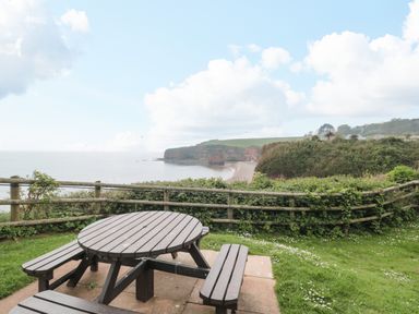 A wooden picnic table and benches on grass overlooking a coastline with cliffs and the sea at The Retreat in Otterton
