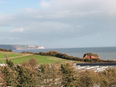A coastal landscape with green fields trees a rocky hill and buildings near the sea at The Retreat in Otterton