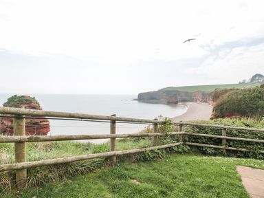 A coastal view with a wooden fence overlooking a beach and cliffs at The Retreat in Otterton