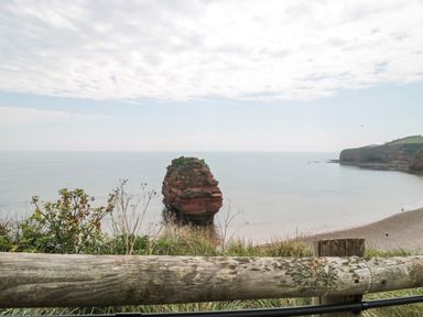 A coastal view with a large rock formation in the sea and a pebble beach with cliffs in the background at The Retreat in Otterton